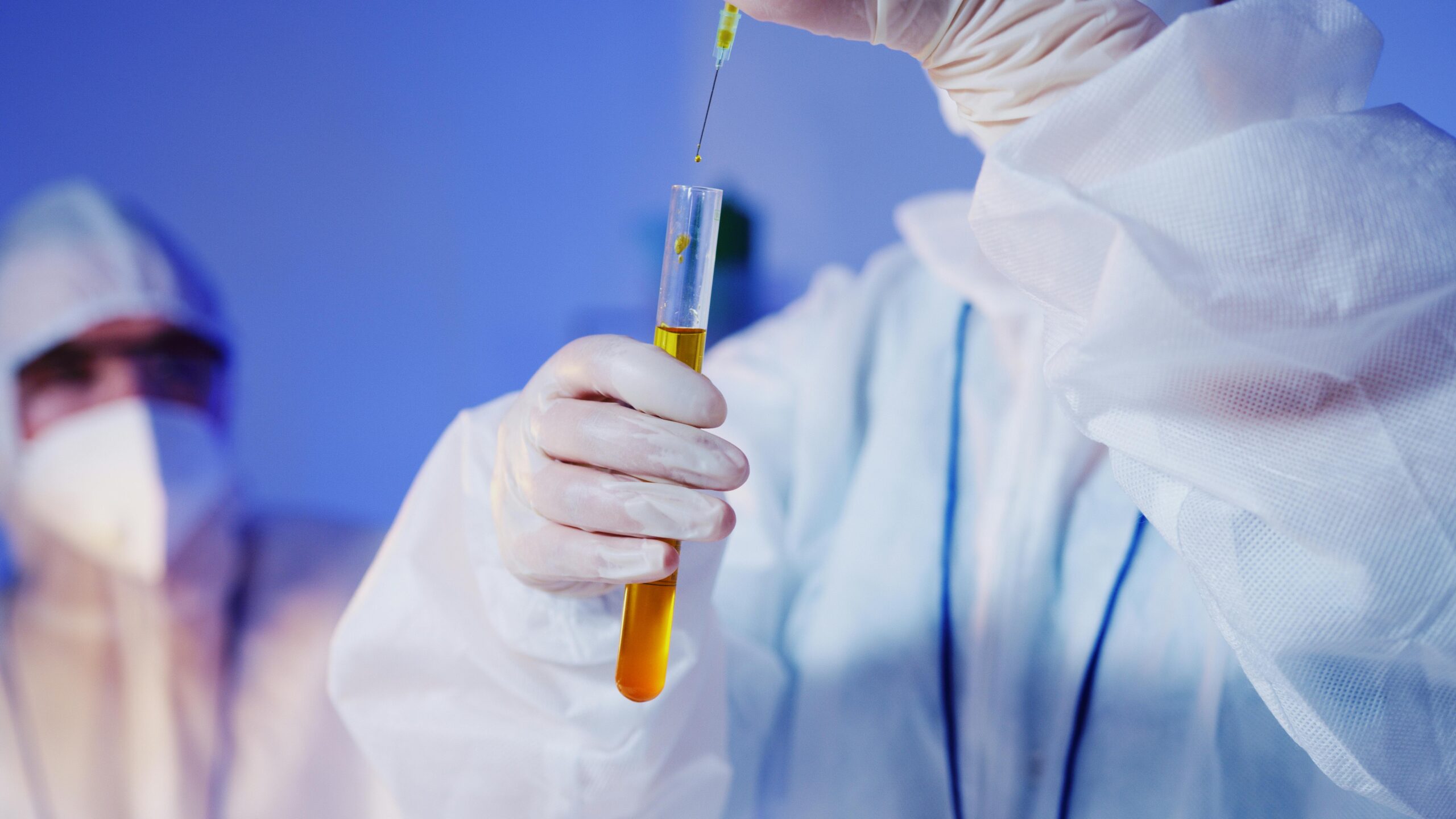 Scientist in protective gear conducting a test with a test tube in a laboratory setting.